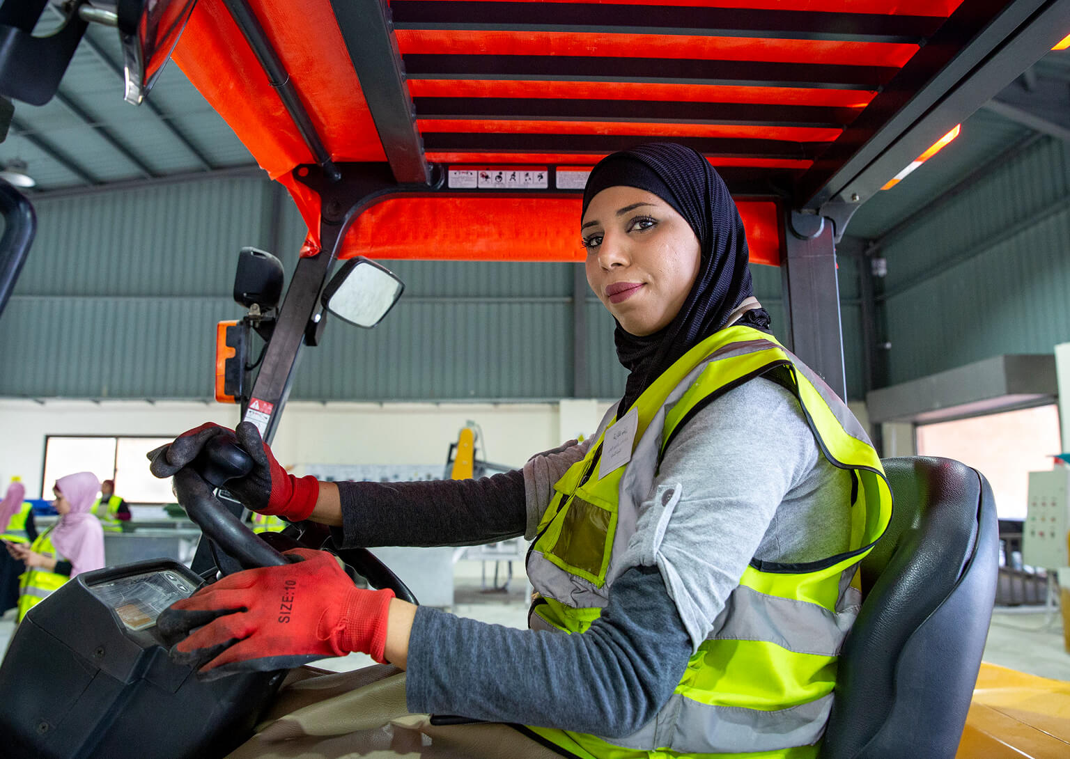 Woman wearing gloves and a high vis vest driving a tractor.